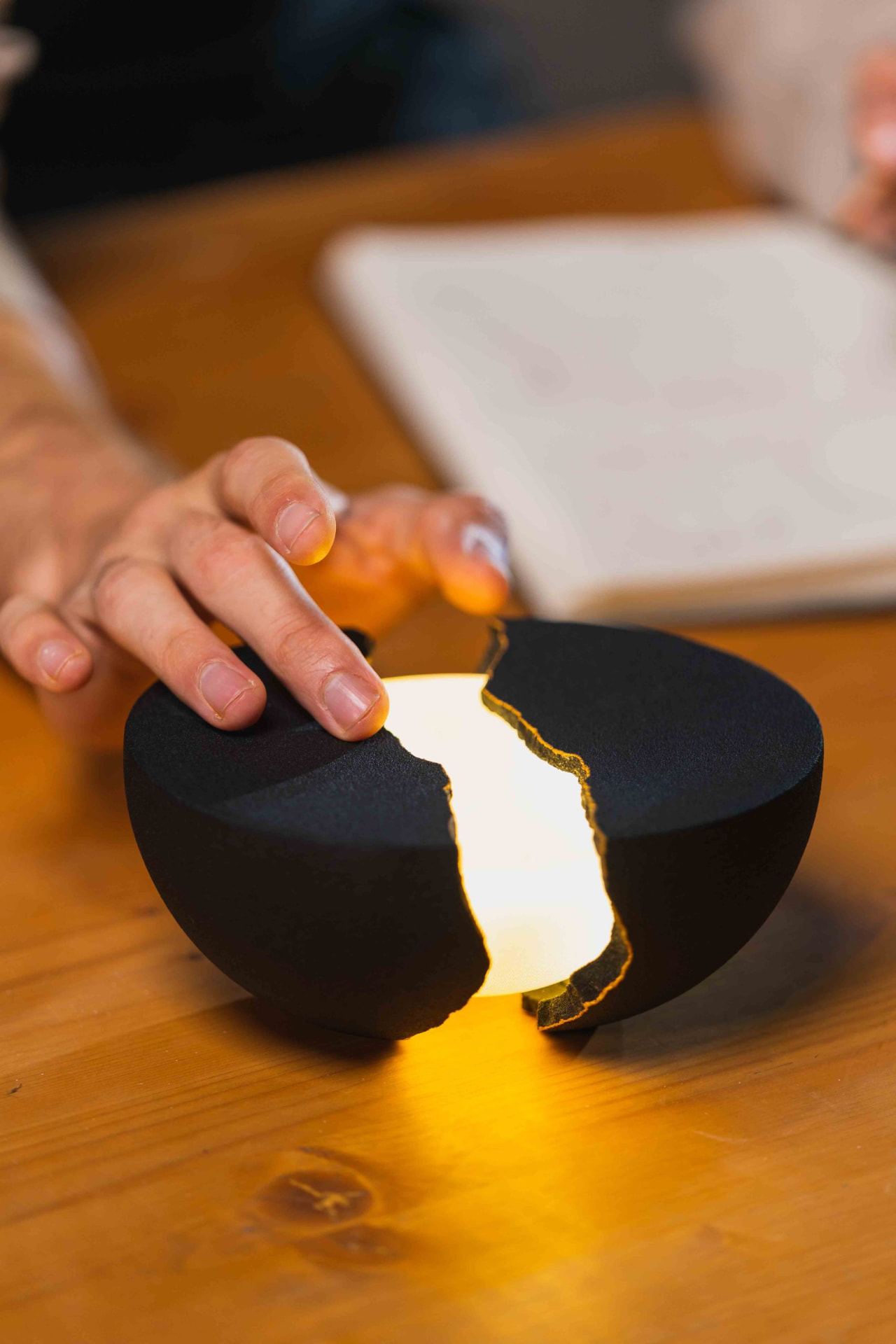 Close-up of a matte-black split-hemisphere lamp glowing amber on a wooden tabletop