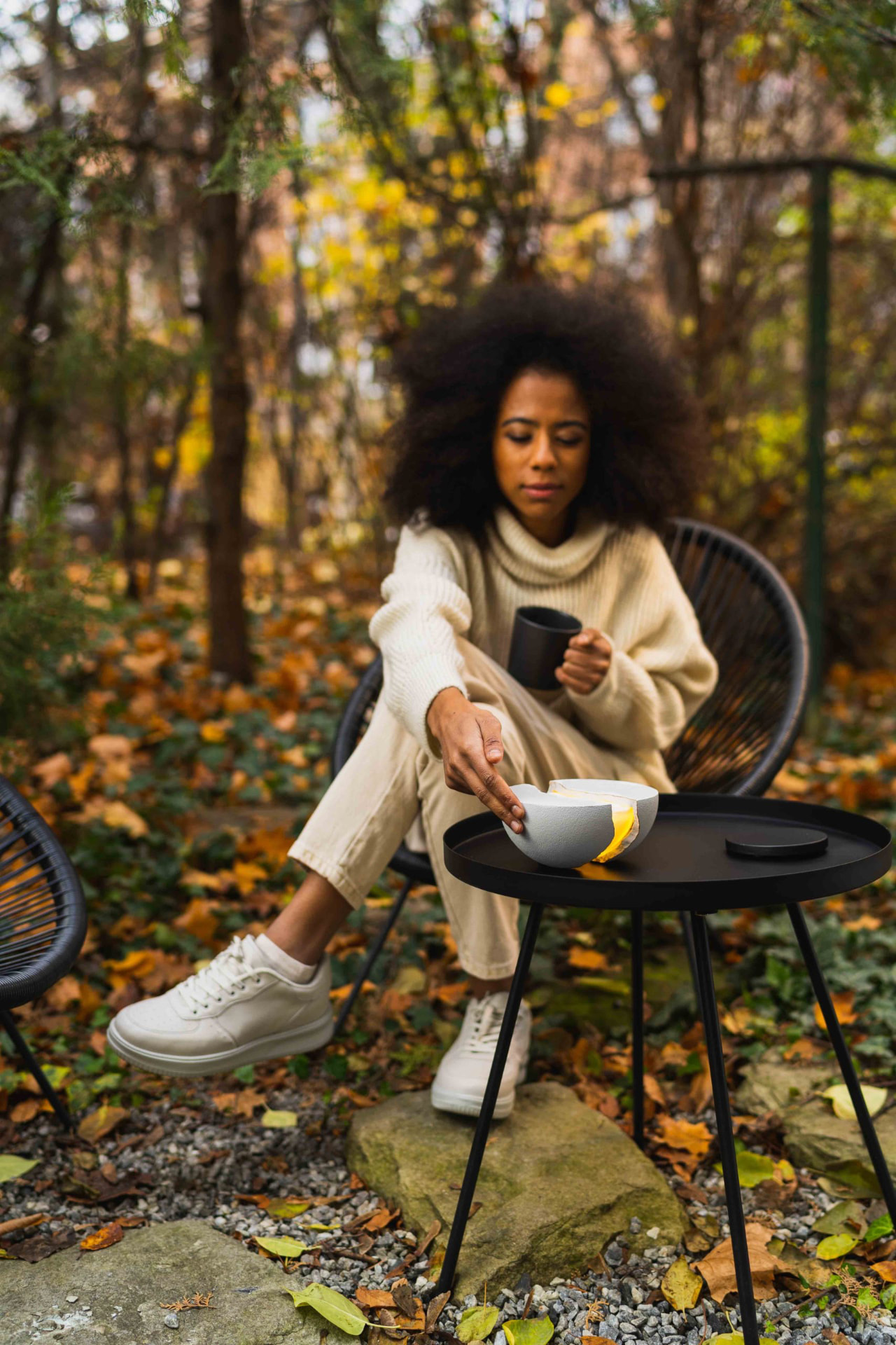 Woman seated outdoors in autumn beside a glowing grey split-hemisphere lamp on a black side table